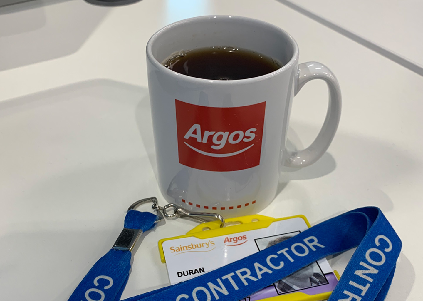 An Argos mug and Sainsbury's Argos contractor lanyard on a desk