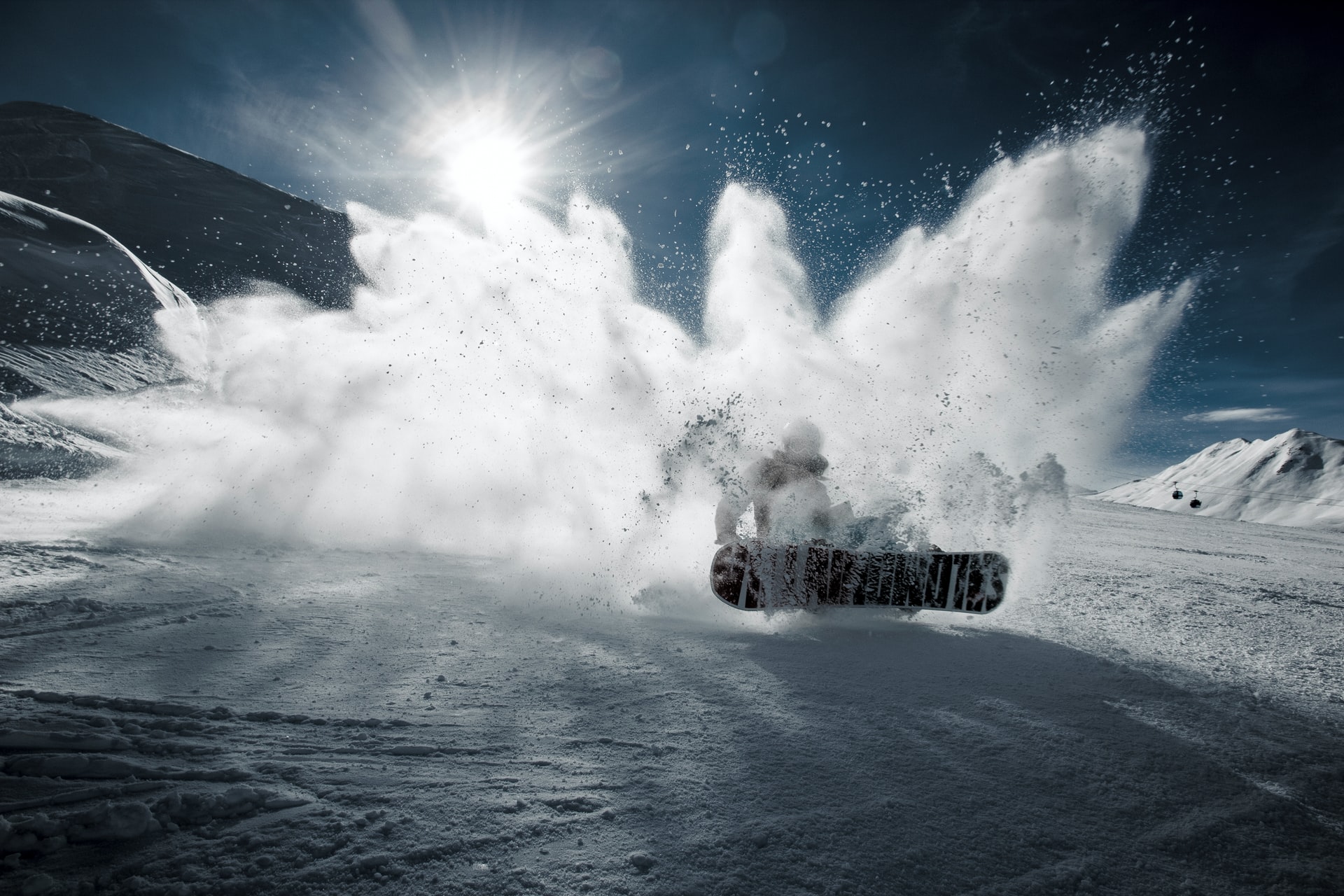 A snowboarder kicking up a cloud of powder on a sunlit ski slope