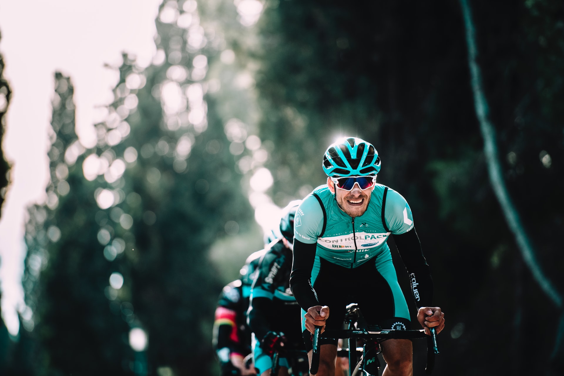 A cyclist in Wiggle team kit riding past trees, lit by low sun